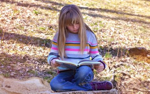 immagine di bambina che legge un libro per evocare il tema della lettura ad alta voce, al centro del bando Ad alta voce 2023, lanciato dal Centro per il libro e la lettura