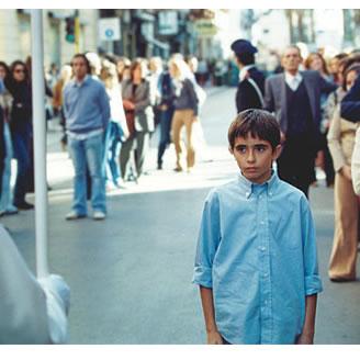 immagine con in primo piano un bambino straniero e sullo sfondo due file di adulti lungo una strada