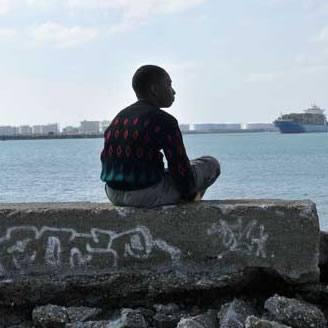 particolare di una scena del film Miracolo a Le Havre in cui il ragazzo è seduto su un muretto, di spalle, e scruta il mare